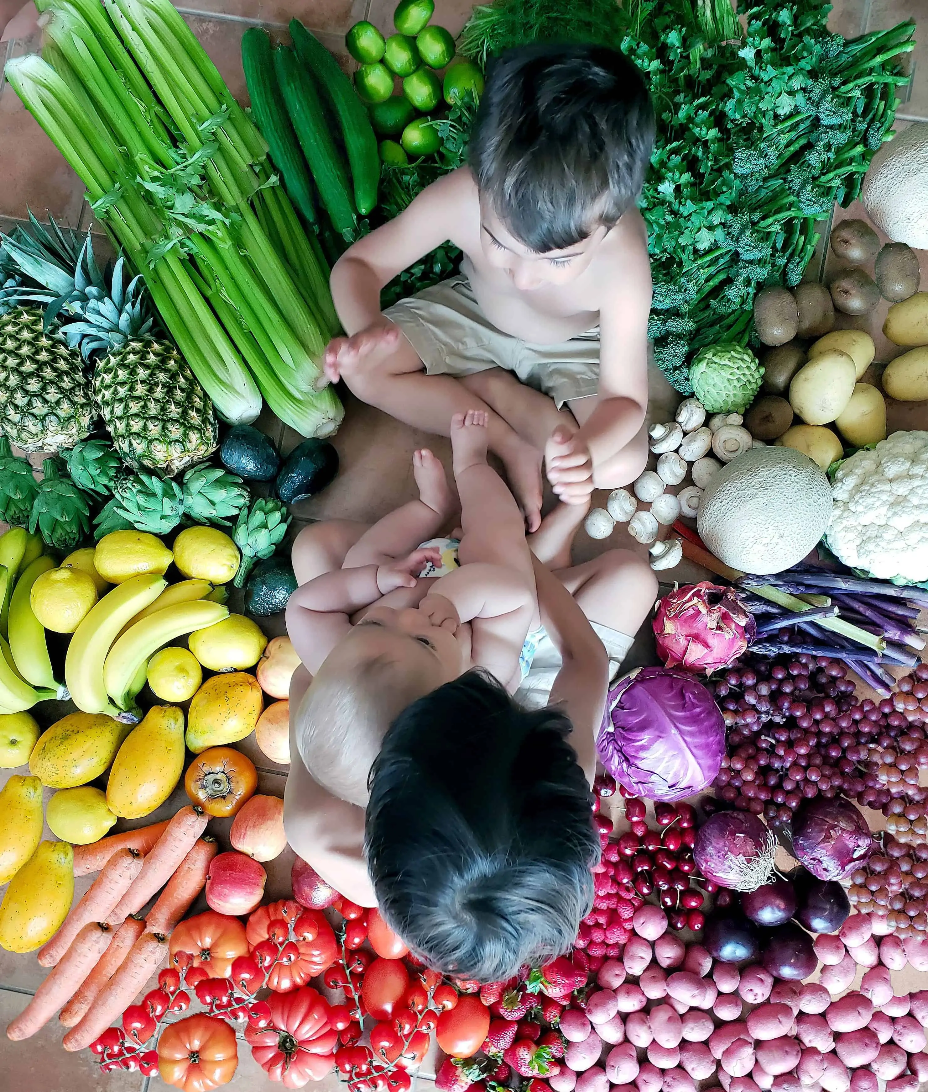 3 young kids sitting together sourounded by healthy raw whole foods. Image is for tips on how to deal with picky eaters.
