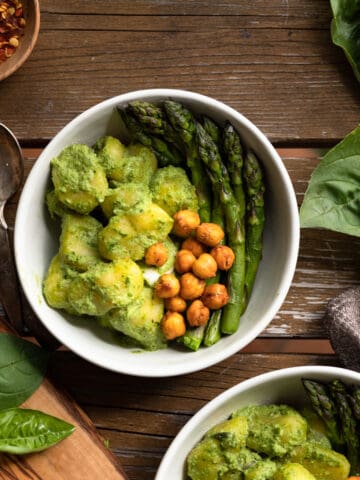 Top down view of a bowl of gnocchi topped with a pesto sauce made without nuts. There is also roasted chikcpeas and aspargus on the plate. The image is to show what the sauce should look like and it is for a recipe post on how to make a nut-free and vegan pesto sauce.