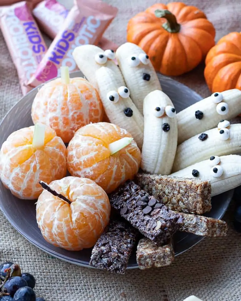 plate of Halloween snack ideas for kids with banana ghosts and tangerine pumpkins