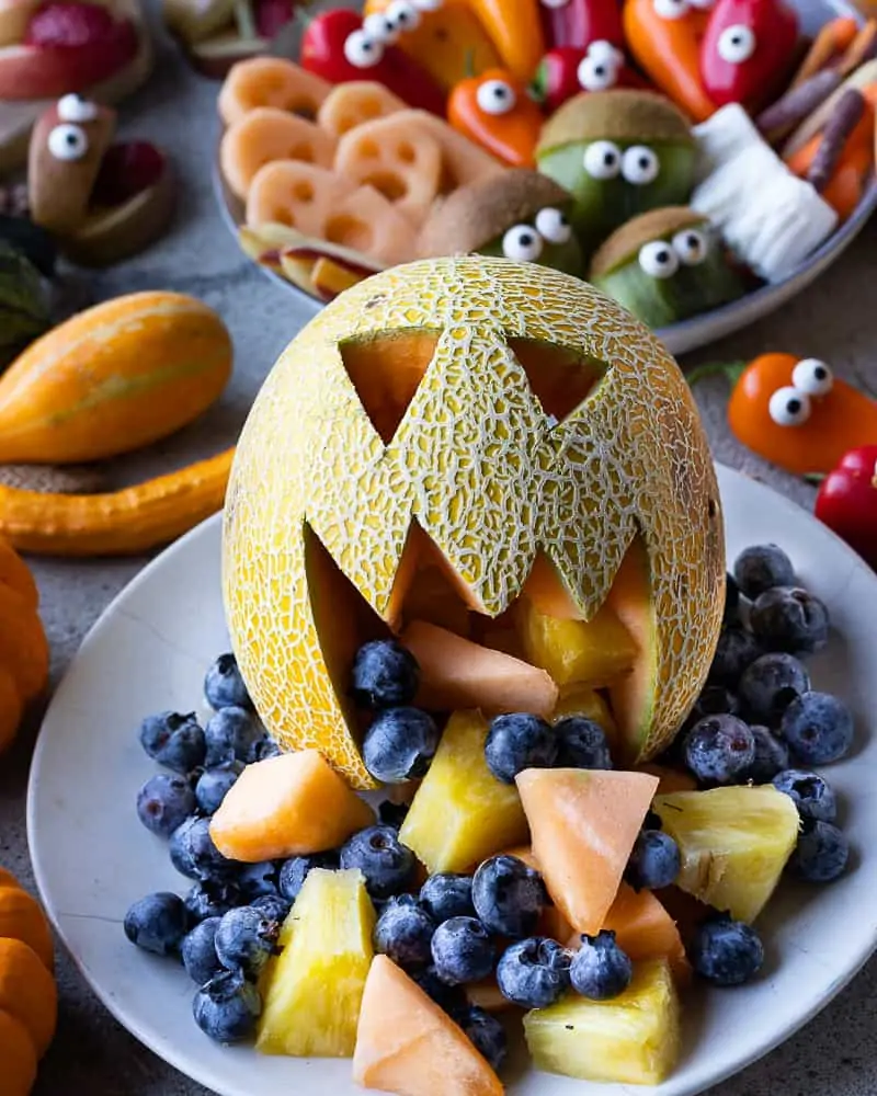 Melon cut into a jack'o'latern with fresh fruit coming out the mouth