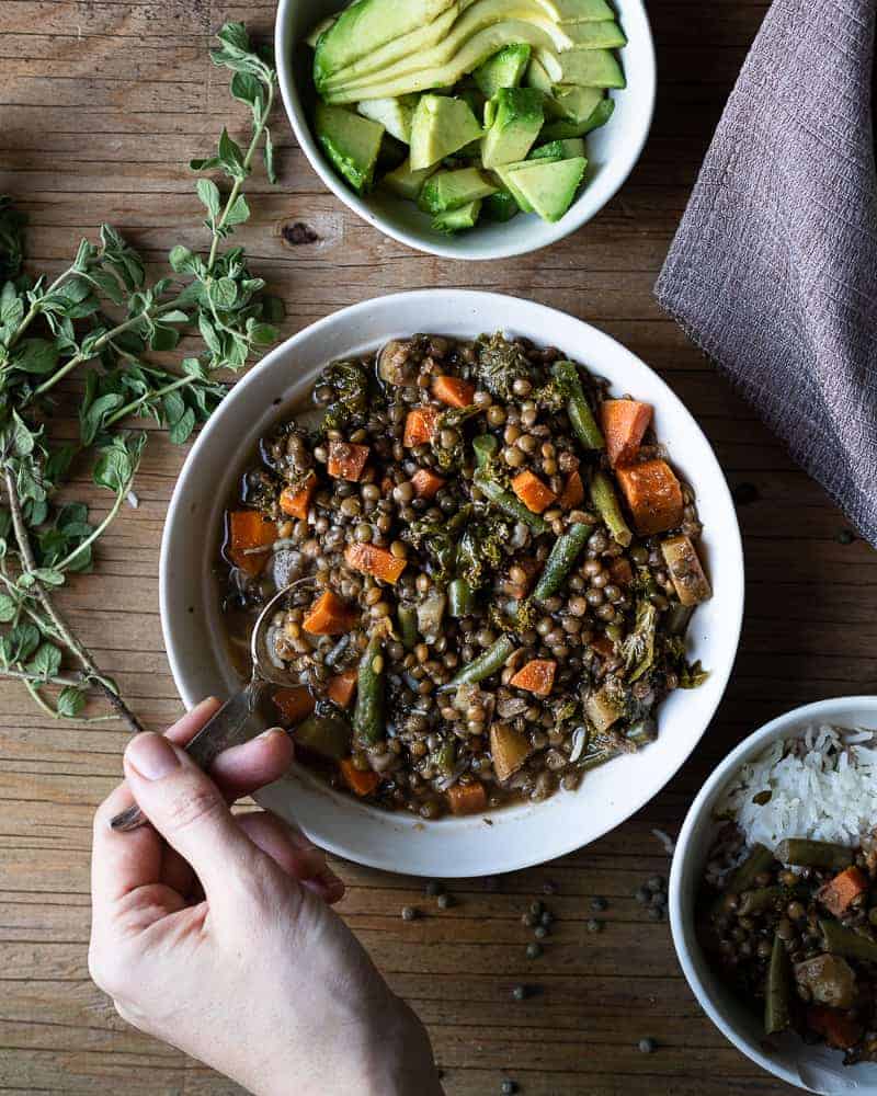 bowl of lentil stew with a hand scooping up a bite