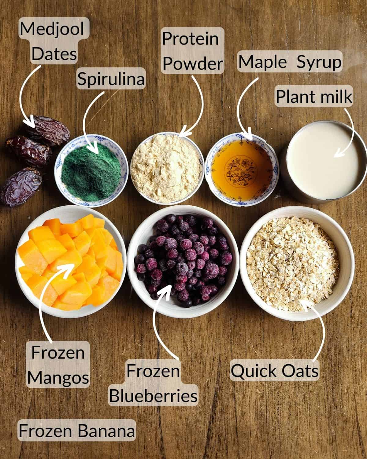 Ingredient image for making high protein overnight oatwith water. Image shows quick oats, maple syrup, protein powder, spirulina, dates, mangos, blueberries and coconut milk