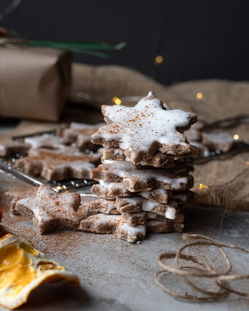 Stack of german cinnamon star cookies with twinkly lights in the background