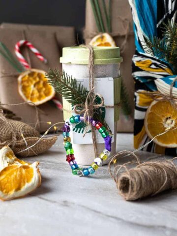 Resuable mug decorated with twine, a coffee card and a bead bracelet surrounded by other presents wrapped in recycled paper