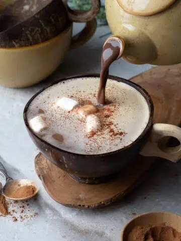 hot chocolate being poured from a pot into a cup
