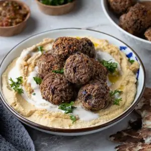 Bowl of hummus topped with egg-free vegan eggplant meatball and parsley. The plate is sitting on a white countertop.