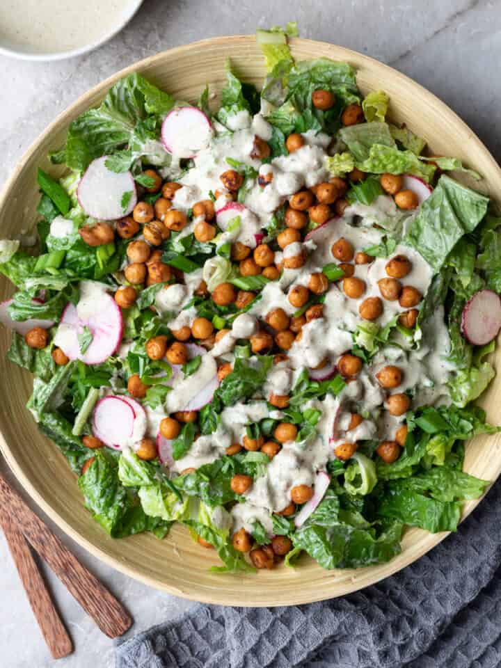 Image for a recipe post on making gluten-free vegan Caesar salad dressing. The image has a big bowl of Caesar Salad topped with crispy chickpea croutons and lemon slices