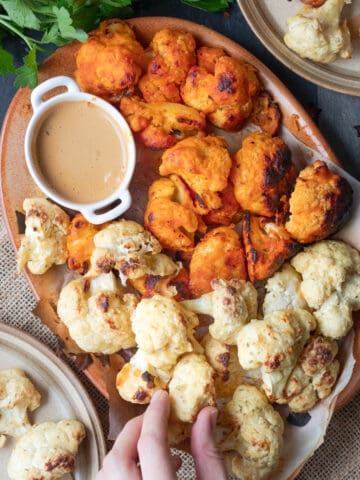 Image of a platter of cauliflower wings to show that this recipe makes two flavors. There is a buffallo wing and a salt and vinegar cauliflower wing. There is also a spicy peanut sauce in the corner of the platter.