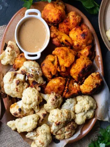Image of a platter of cauliflower wings to show that this recipe makes two flavors. There is a buffallo wing and a salt and vinegar cauliflower wing. There is also a spicy peanut sauce in the corner of the platter.