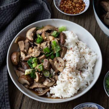 bowl of sauteed mushrooms with rice and green onions on a wooden table