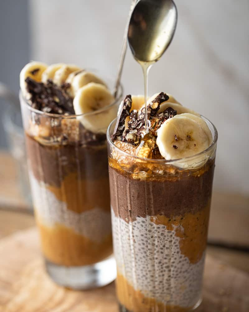 Angle shot of 2 cups full of chocolate and peanut butter chia pudding with a honey drizzle