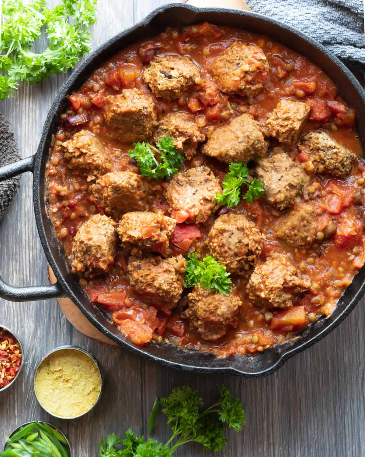 birds eye view of a cast iron pan with high protein quinoa meatballs  in a marinara sauce and a wooden spoon 