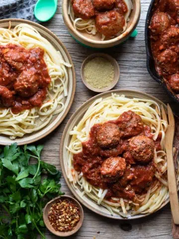 Top-down view of 3 plates of spaghetti and vegan gluten free meatballs and a cast iron pan full of marinara sauce with meatballs.