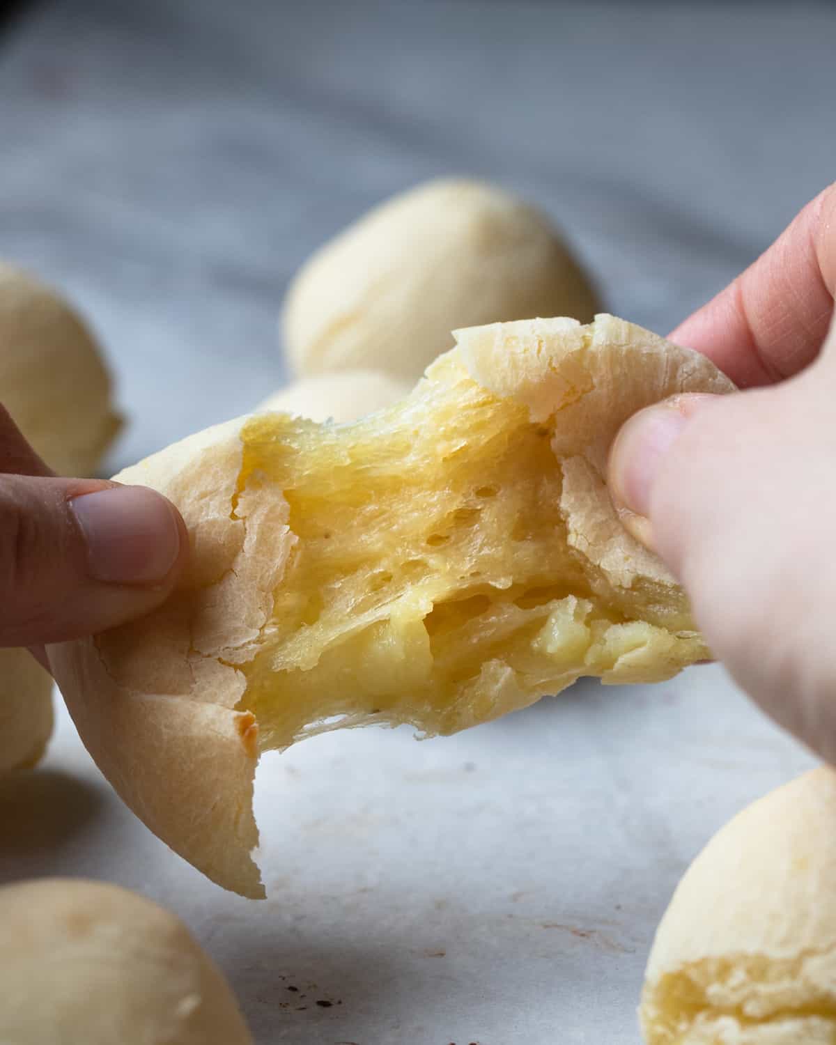 Image of a vegan pao de queijo being strecthed apart to show the stretchy interior of the finished and baked recipe.