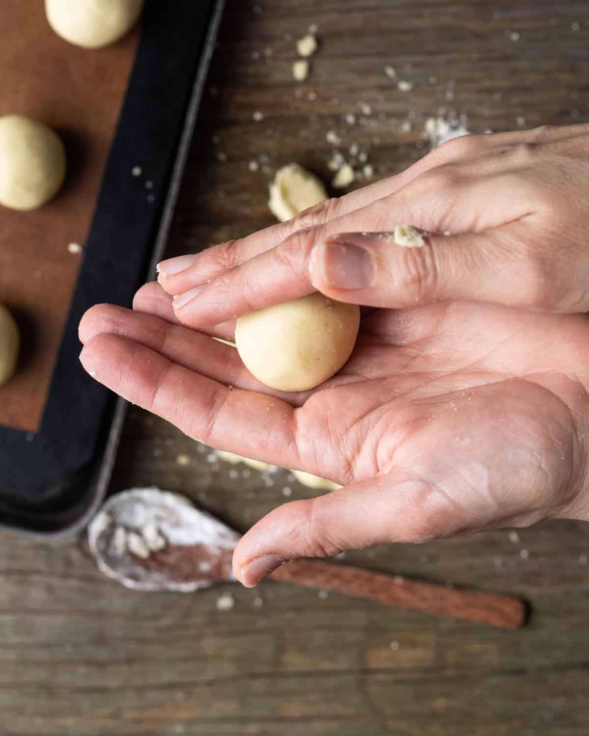 Image of a human hand rolling pao de queijo dough into small balls.