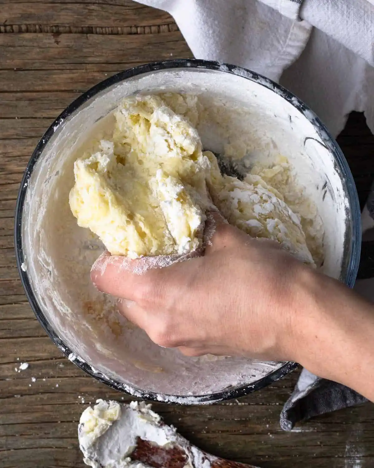 Prep shot for a recipe for pao de queijo recipe. The image shows a bowl of tapiocabatter being kneaded by a human hand.