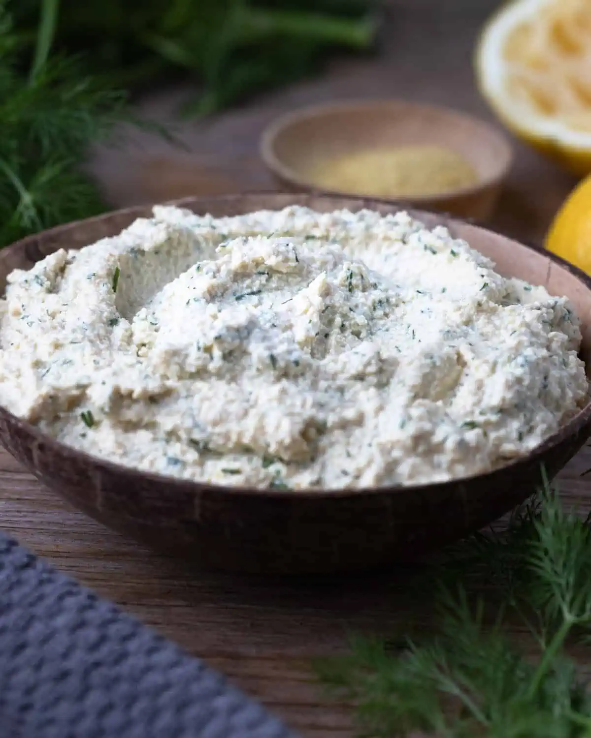 A close-up of a wooden bowl filled with tofu cheese ricotta and dill.