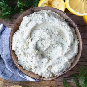 A wooden bowl of easy and quick tofu cheese ricotta. The bowl is surrounded by fresh lemon and dill.