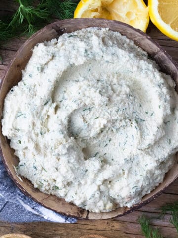 A wooden bowl of easy and quick tofu cheese ricotta. The bowl is surrounded by fresh lemon and dill.