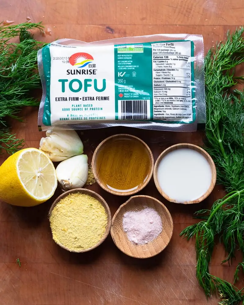 Wooden cutting board with ingredients for making tofu cheese. The image shows tofu, spices and lemon juice. 