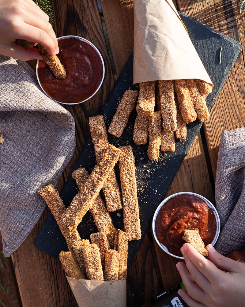 Birds eye view of vegan tofu fingers with a almond crust for a gluten free recipe. Fingers are being dipped in Ketchup.