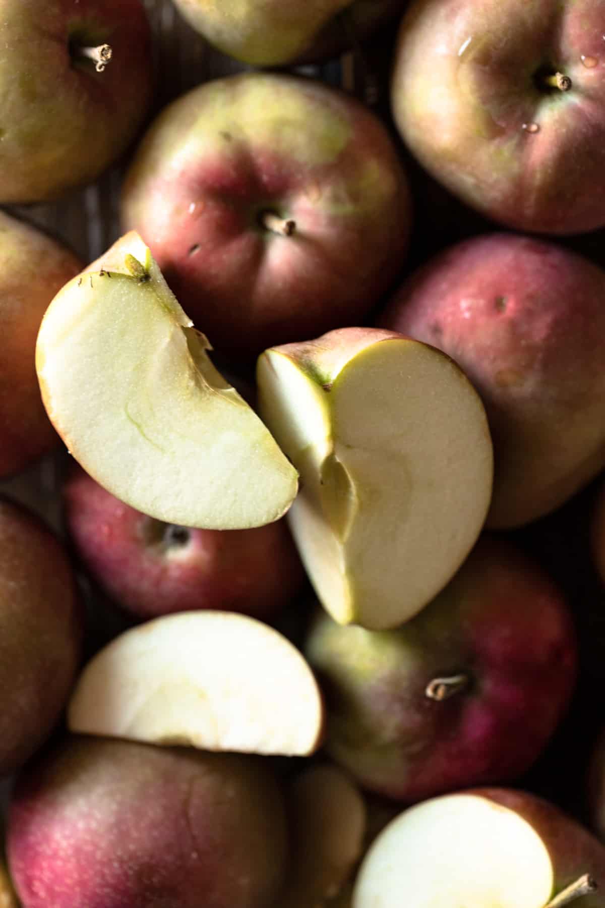 Closeup image of red McIntosh apples, some are cut into quarters and some are whole.