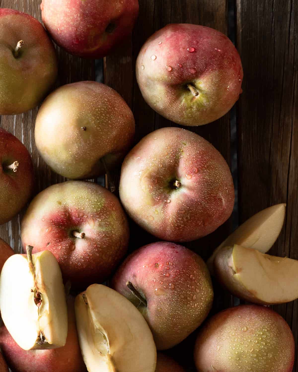 Closeup image of washed red McIntosh apples, some are cut into quarters and some are whole.