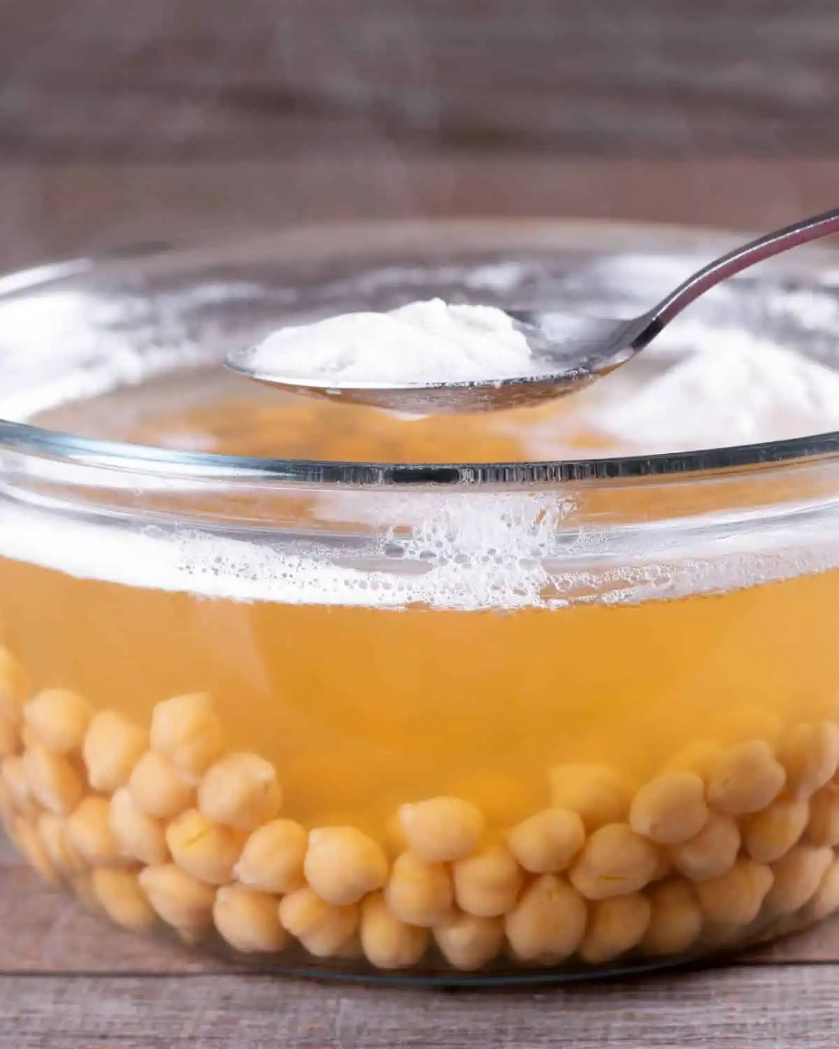 Glass bowl of chickpeas and chickpea liquid to show what Aquafaba is. The image is for a recipe post on how to use aquafaba in place of eggs.