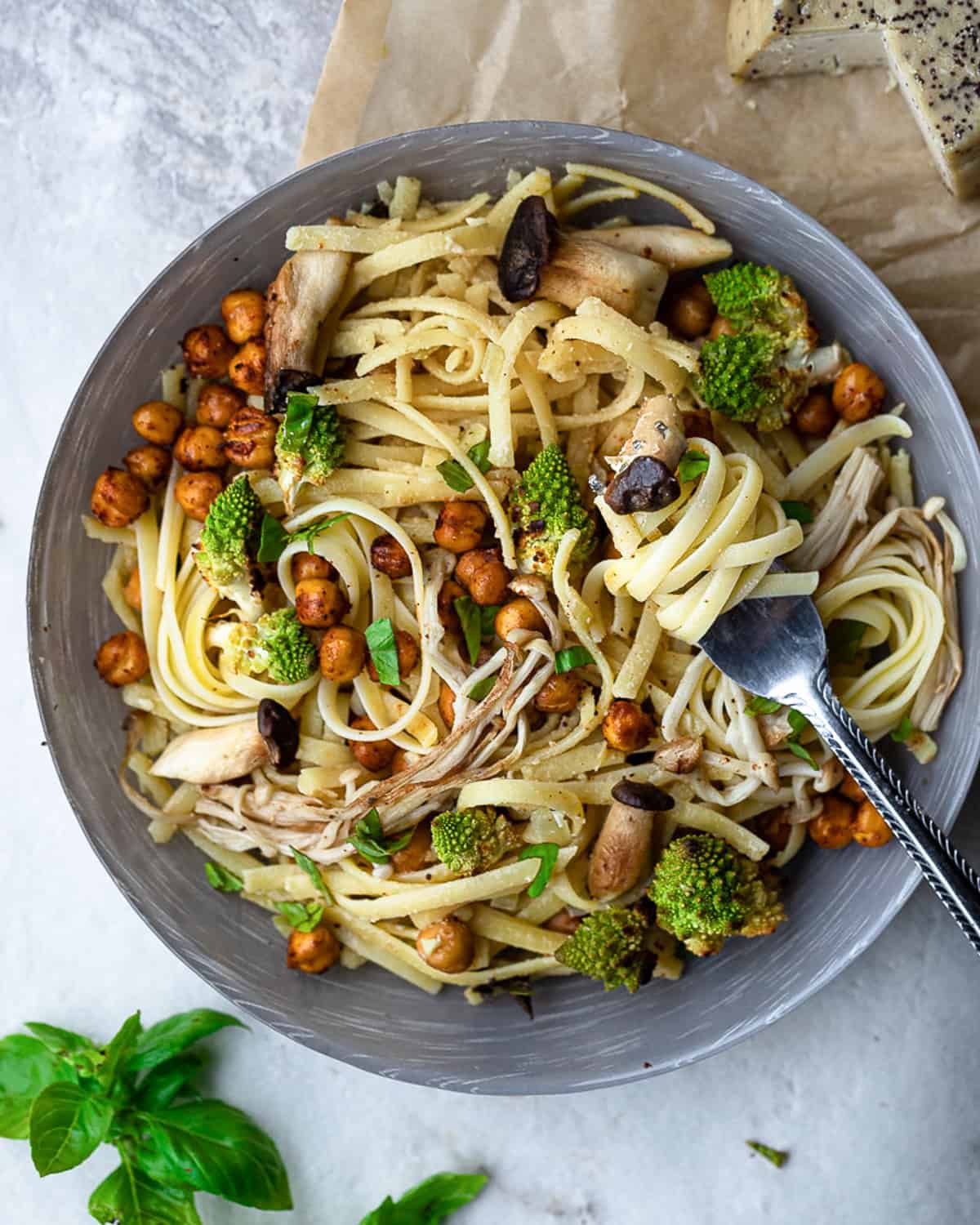 Bowl of vegan creamy pasta sauce topped with roasted mushrooms, chickpeas, and romanesco cauliflower. There is a fork resting on the plate twirled in the pasta.