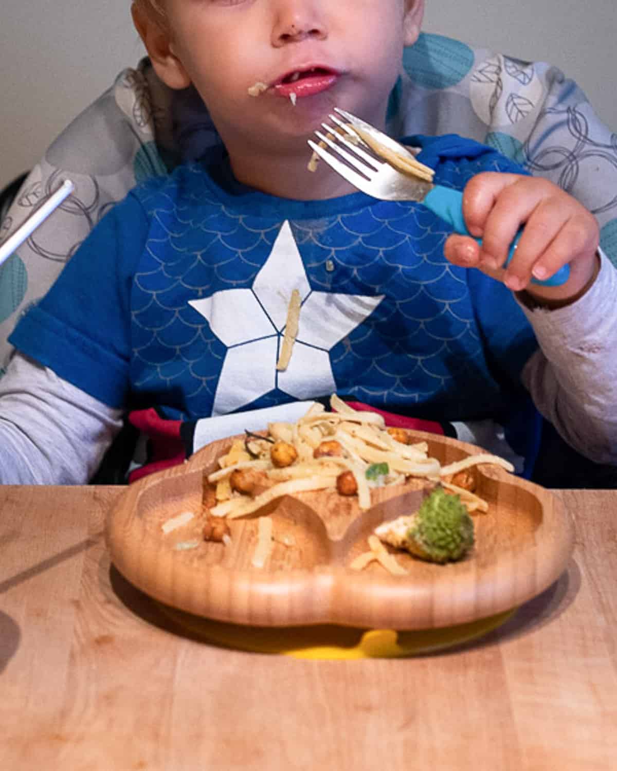 Child eating a plate of Bowl filled with vegan creamy pasta, with chickpeas, and romanesco cauliflower.