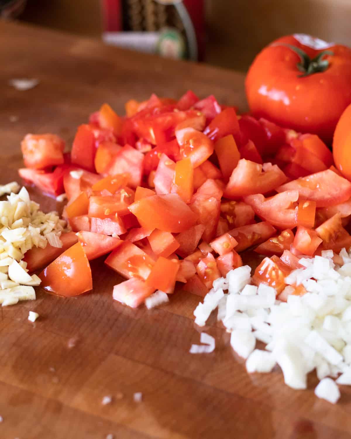 Close up image of a cutting board with cut fresh tomatoes, onions, and fresh garlic. The image is for a recipe post on how to make lasagna