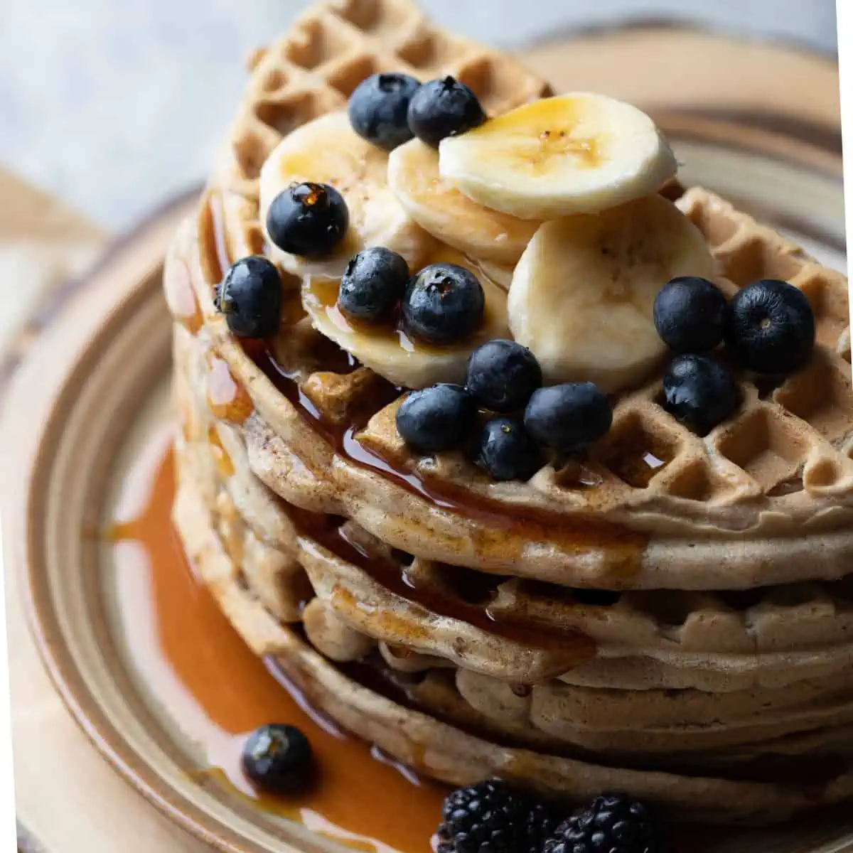 Close up image of a stack of vegan gluten free waffles with fresh fruit on top. the image is to show the fluffy texture of the final product.