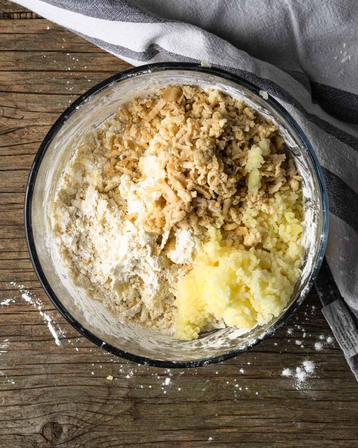 Image of a glass bowl with tapioca flour, mashed potatoes, vegan cheese, salt, and garlic powder. The image is a process shot for how to make Brazilian cheese bread balls.