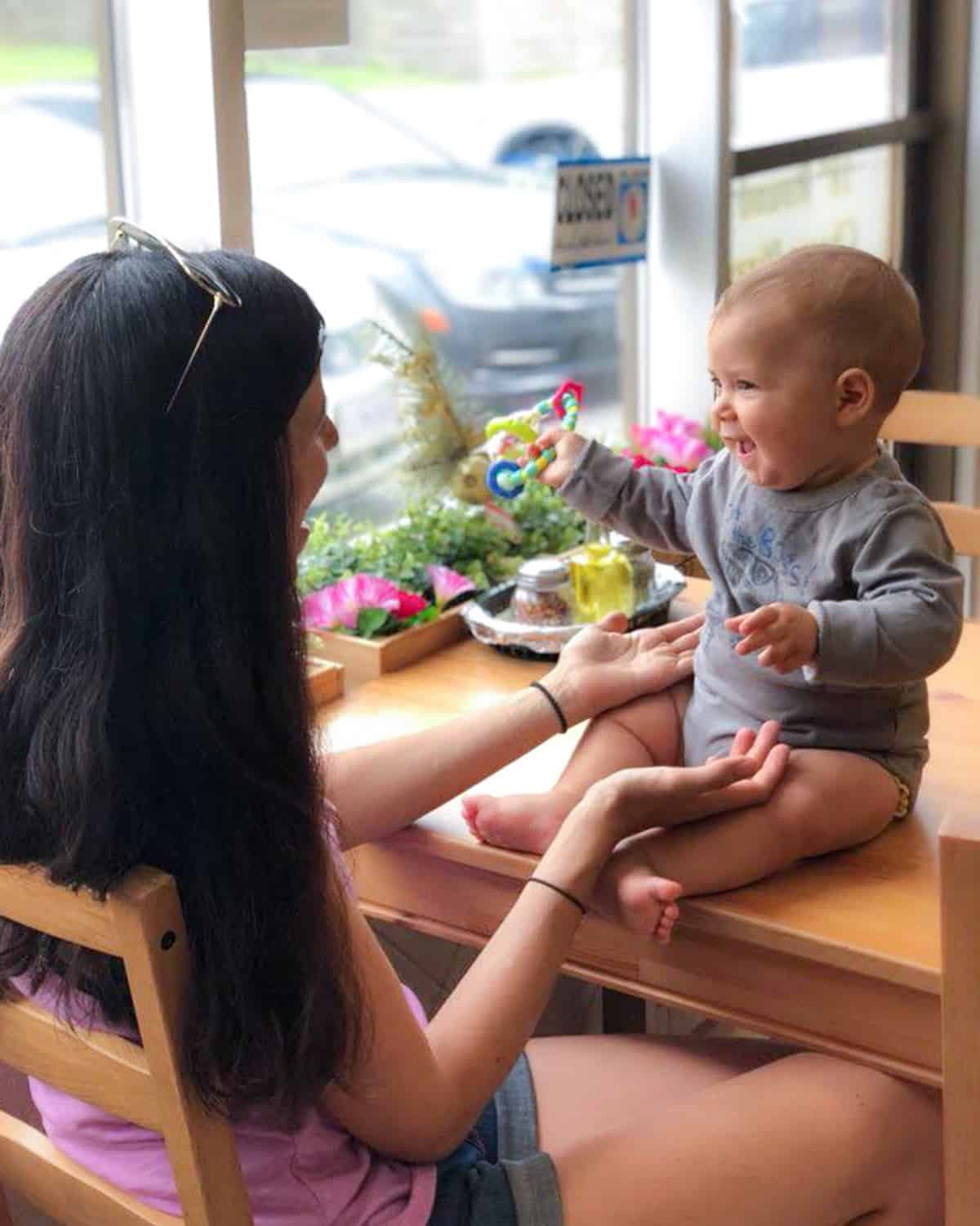 Image of a mother and baby smiling and playing. Baby is sitting on a wooden table and the image of for a blog post talking about the safety of a vegetarian and vegan pregnancy meal plan