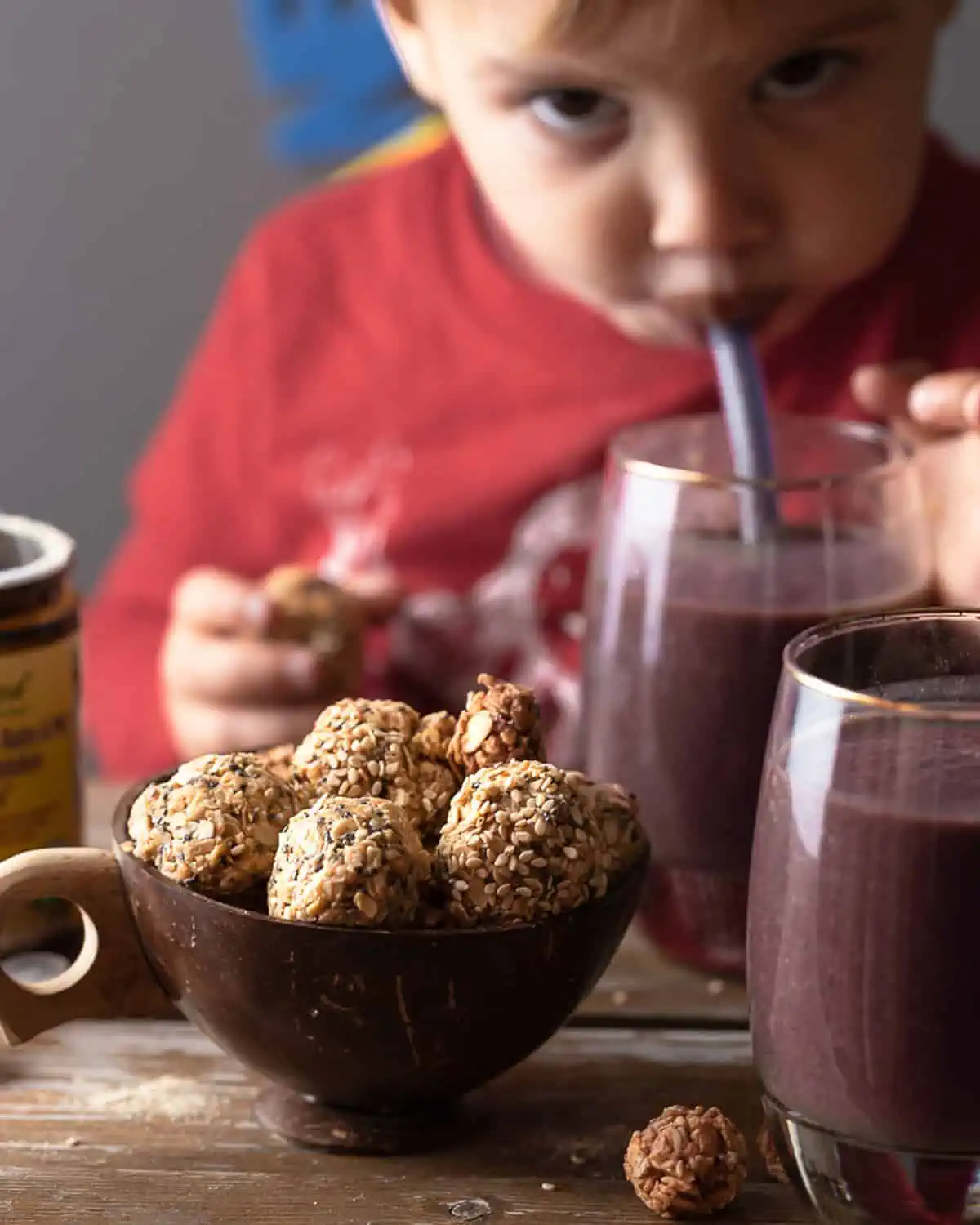 Close up image of oat balls and a smoothie with a 12 month old in the background. Image is for a post on what a toddler eats in a day with dinner ideas.