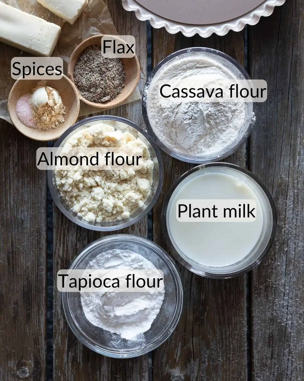 Ingredient image for a recipe post on making gluten free and vegan quiche. The image shows flax, spices, tapioca flour, almond flour, cassava flour, and plant milk.
