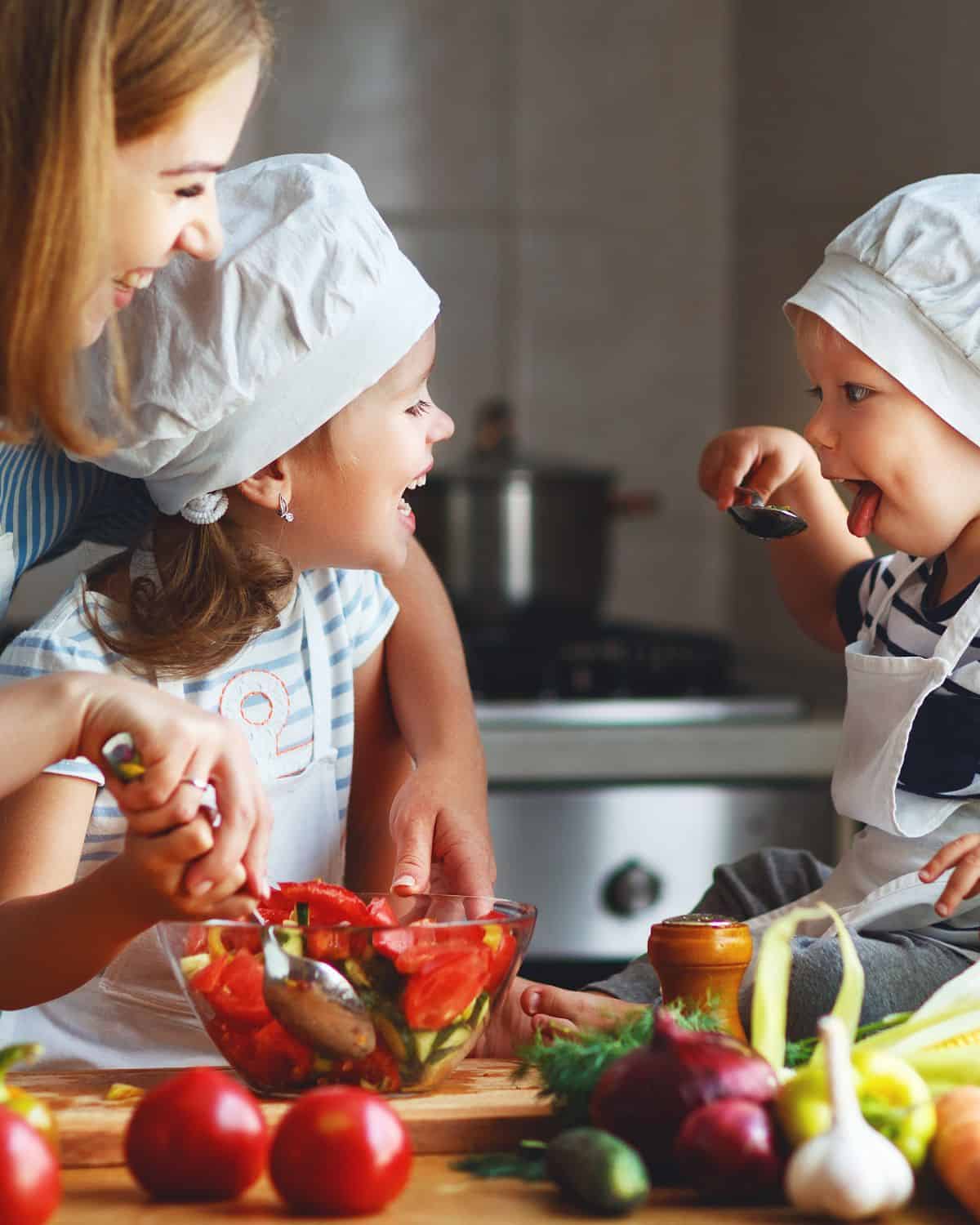 Happy mother with two kids cooking together in the kitchen. Image is for a recipe post on tips and meal ideas for picky eaters.