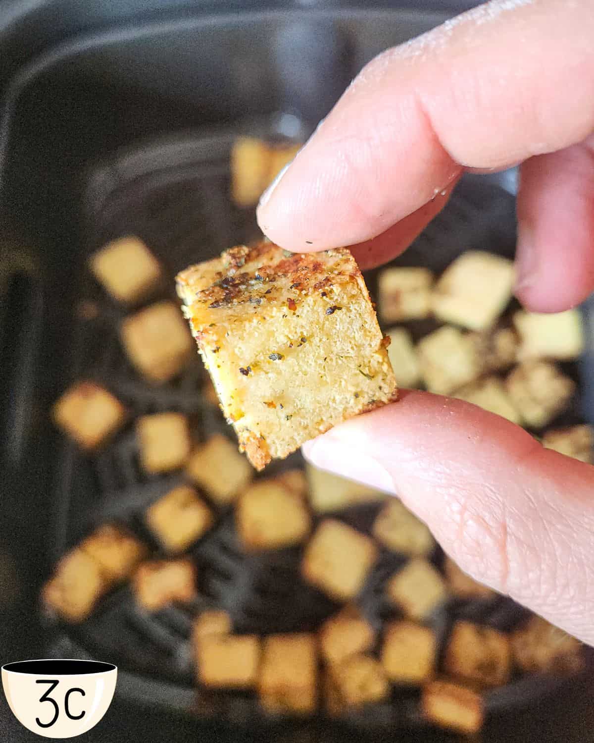 Image showing a close up of cooked tofu in an air fryer to show the texture and how cripsy the tofu should be. 