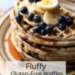Pinterest Pin Image of a stack of gluten free and vegan waffles topped with fresh fruit and maple syrup. The pin is for a recipe post on how to make fluffy gluten free waffles with no eggs. Text overlay reads Fluffy Gluten Free Waffles.