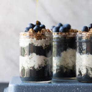 Image of a 3 mason jars with layers of a high protein smoothis and overnight oats topped with fresh granola and blueberries. The image is to show what the final recipes should look like.