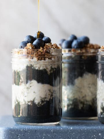 Image of a 3 mason jars with layers of a high protein smoothis and overnight oats topped with fresh granola and blueberries. The image is to show what the final recipes should look like.