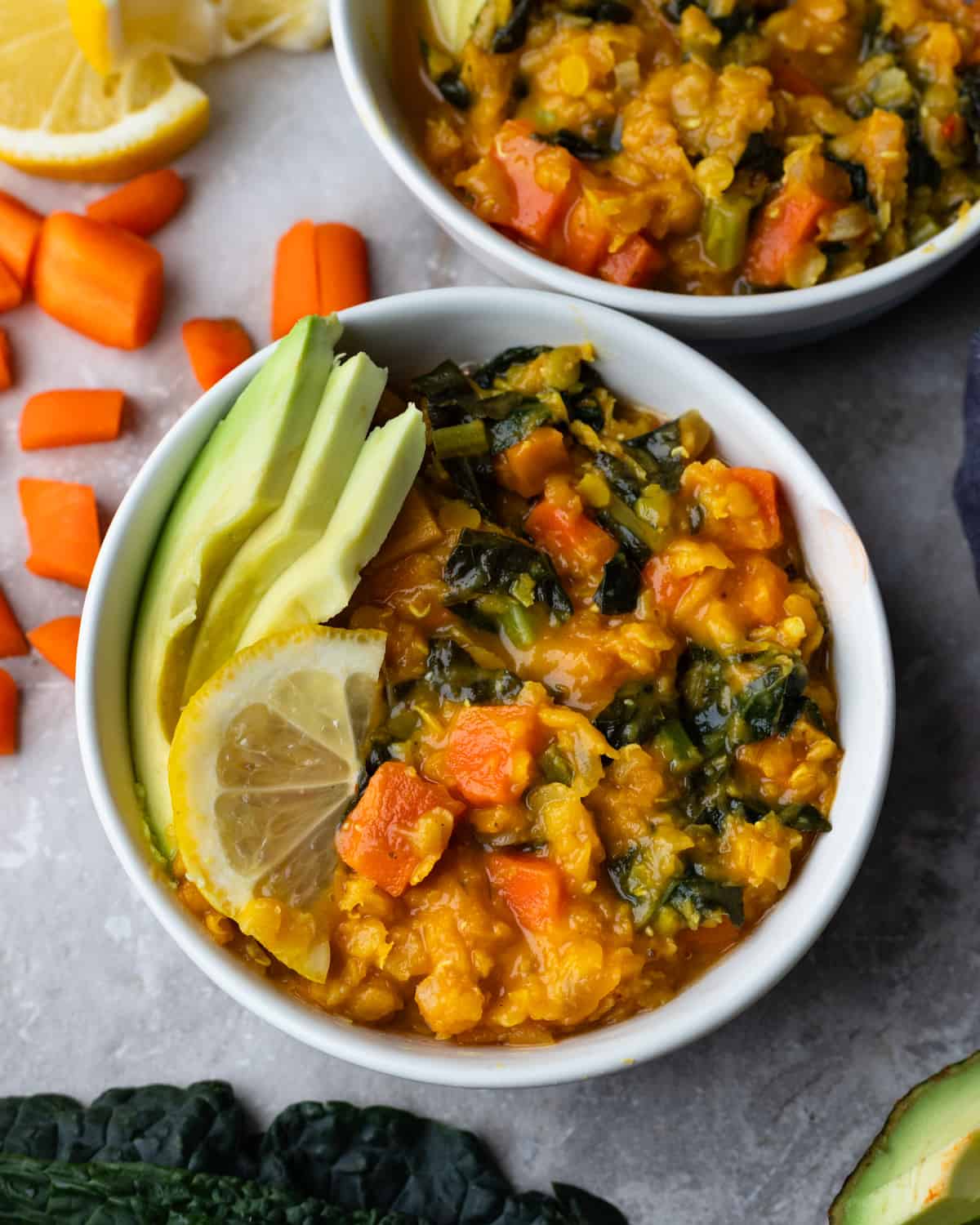 Close up image of 2 bowls full of a carrot and kale red lentil stew. The recipe is keto-friendly and made in the instant pot. The stew is topped with fresh lemon and avocado.