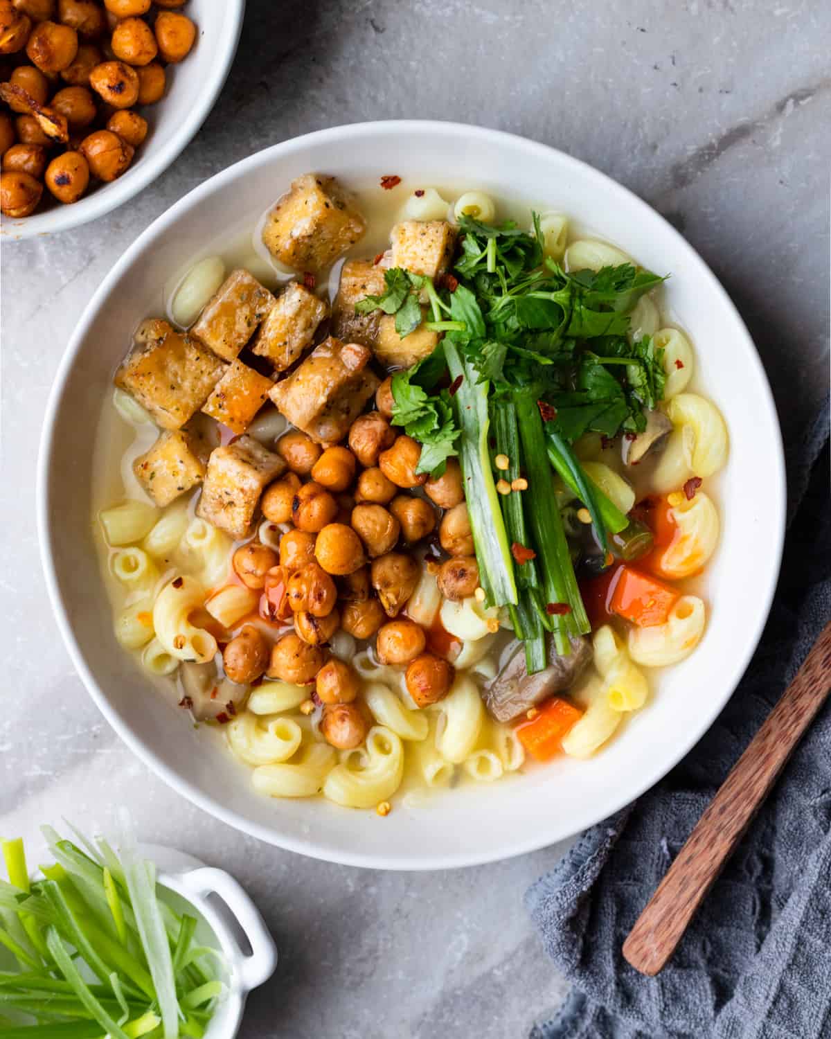 Top down image of a bowl of vegetable soup made with gluten free noddles topped with cripsy baled tofu and chickpeas.