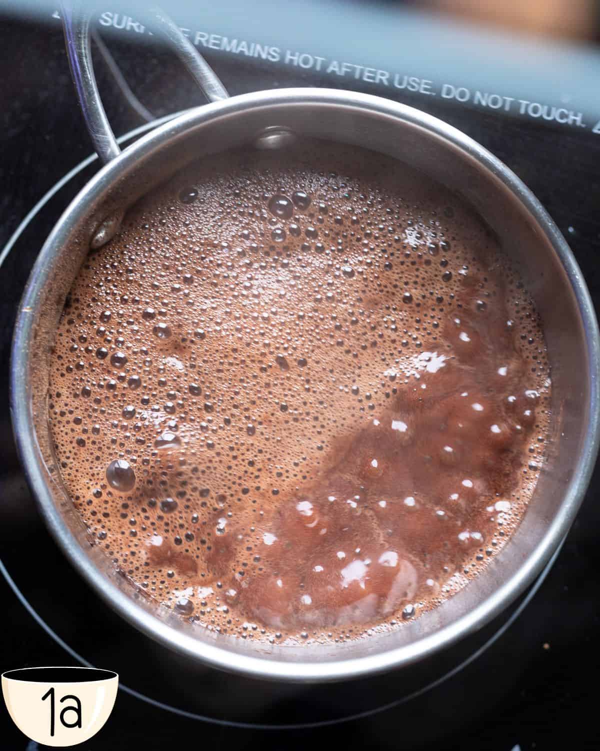 Vegan brigadeiro mixture being cooked over low heat in a pan. The mixture is just coming to a boil.