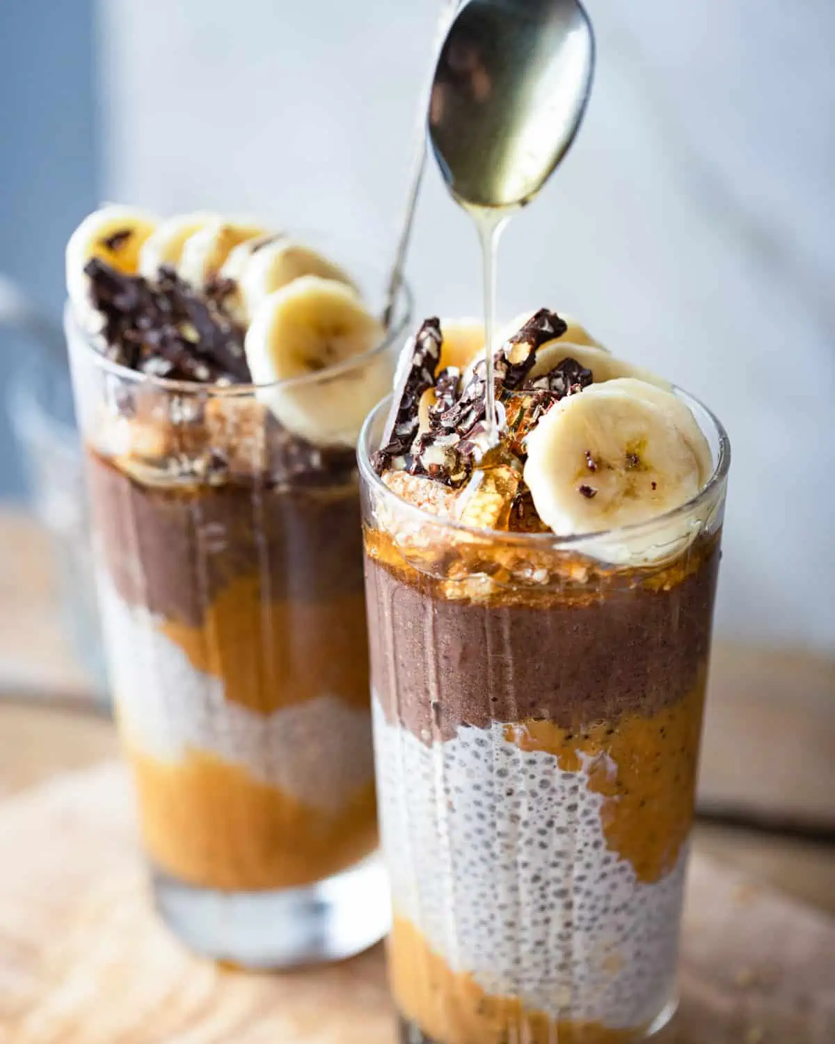 Image of 2 cups with layers of vanilla and chocolate chia pudding with peanute butter and maple syrup.