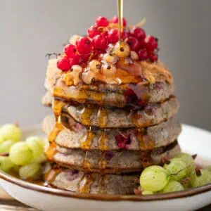 Image of a stack of gluten free vegan buckwheat pancakes topped with fresh currents. There is maple syrup being poured on top of the stack. the image is for a recipe post on how to make fluffy gluten free pancakes .