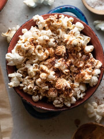 close up image of vegan cimmaon popcorn in a small bowl. The popcorn is topped with butter and fresh ground cinnamon.