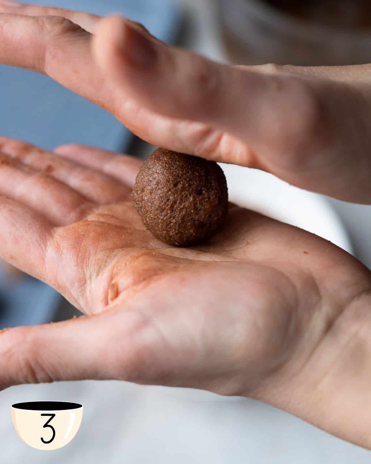 A close-up of a hand shaping the chocolate mixture into a small, round bliss ball, demonstrating a step in preparing this healthy snack for kids.