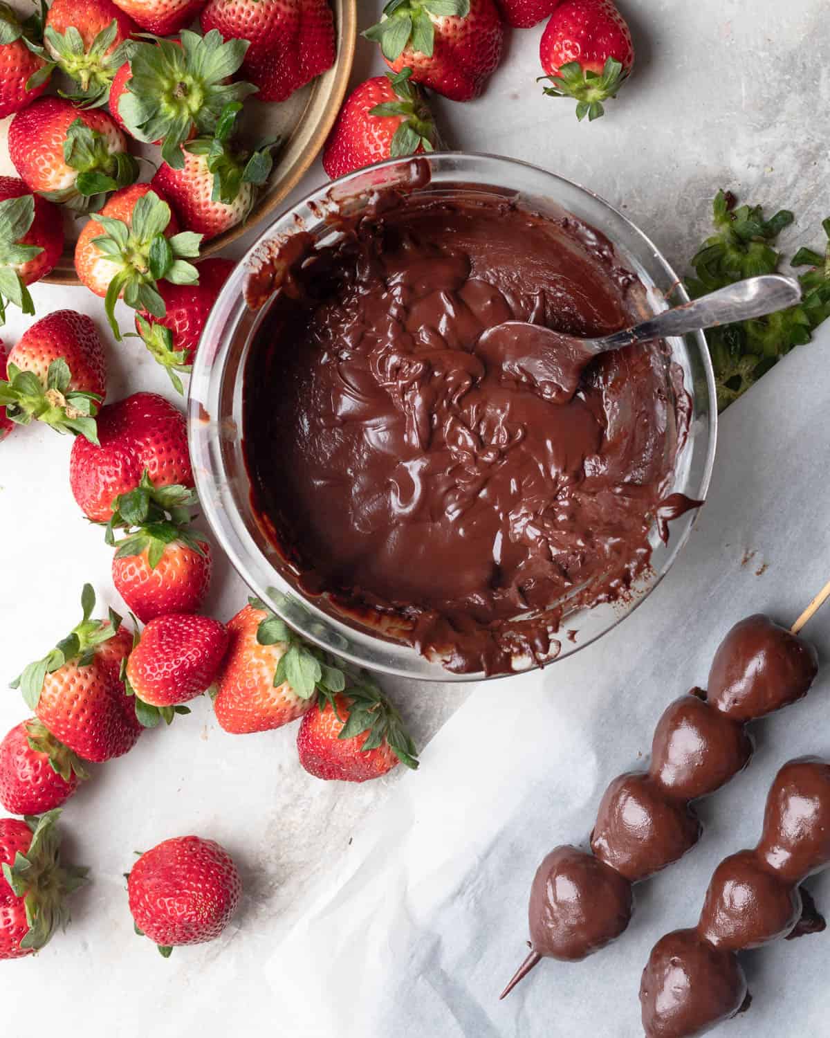 Bowl of vegan chocolate surrounded by fresh strawberries and some already dipped and ready chocolate covered strawberries.