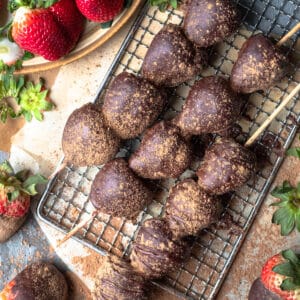 Three skewers of fresh strawberries covered in chocolate and sprinkled with powdered cinnamon.